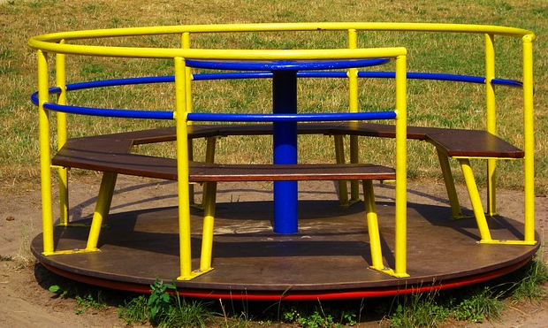 Bild 10: gelb-blaues Karusell mit runder Sitzbank auf brauner Holzdrehscheibe 