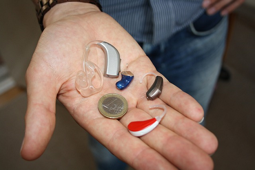 Bild 3: verschiedene Hörgerätemodelle und eine 1 Euro Münze zum Vergleich in der geöffneten Hand eines Mannes